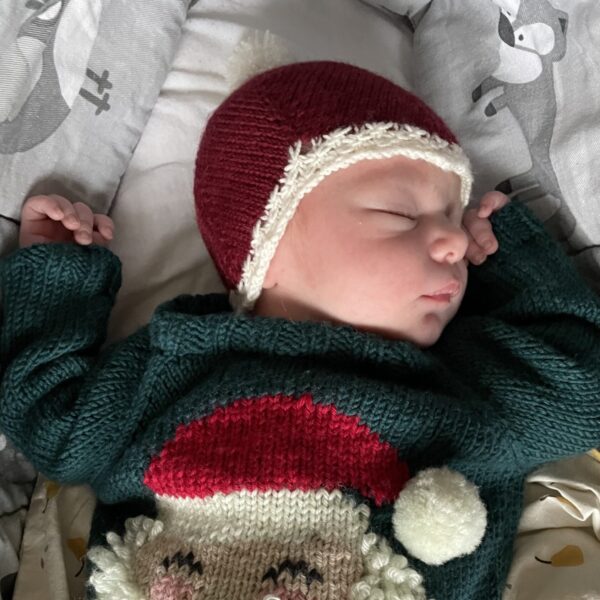 Nyfødt baby i strikket sweater og djævlehue som nissehue